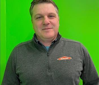 a man wearing a dark grey shirt in front of a green background